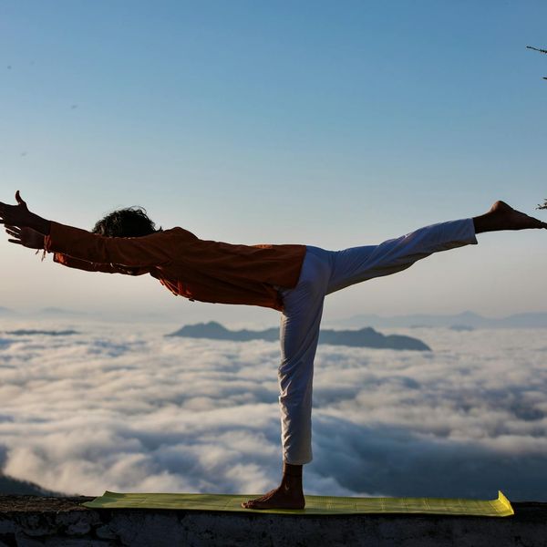 Silhouette of a person in a powerful yoga warrior pose at sunrise.
